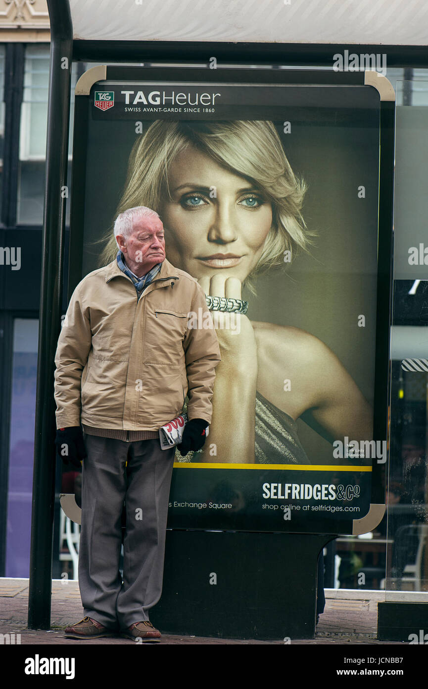 Old man leaning against advertising poster whilst waiting for the bus. Stock Photo