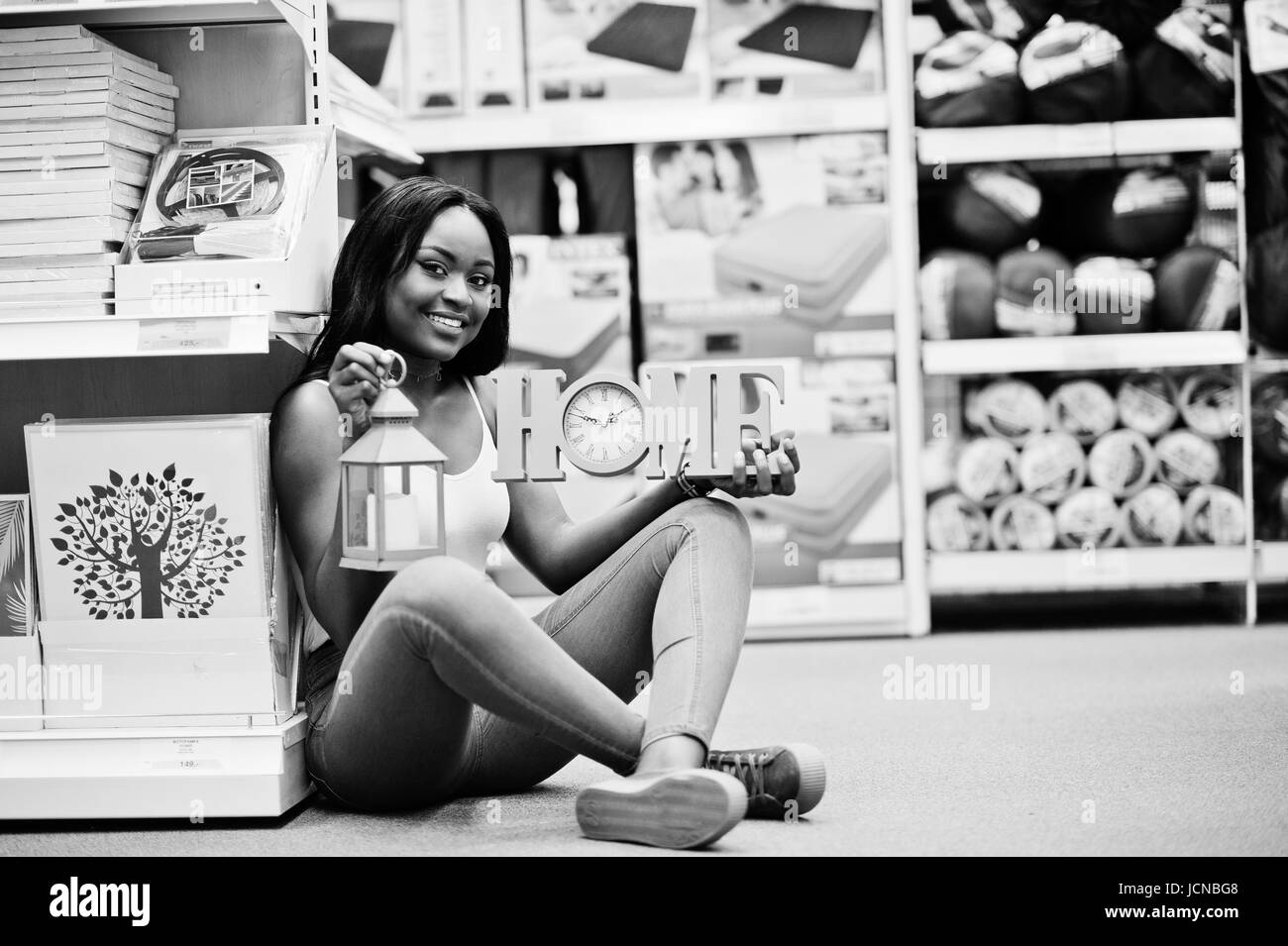 Portrait of a beautiful african american woman sitting on the floor with a home sign and a sconce torch in her hands in the store. Black and white pho Stock Photo