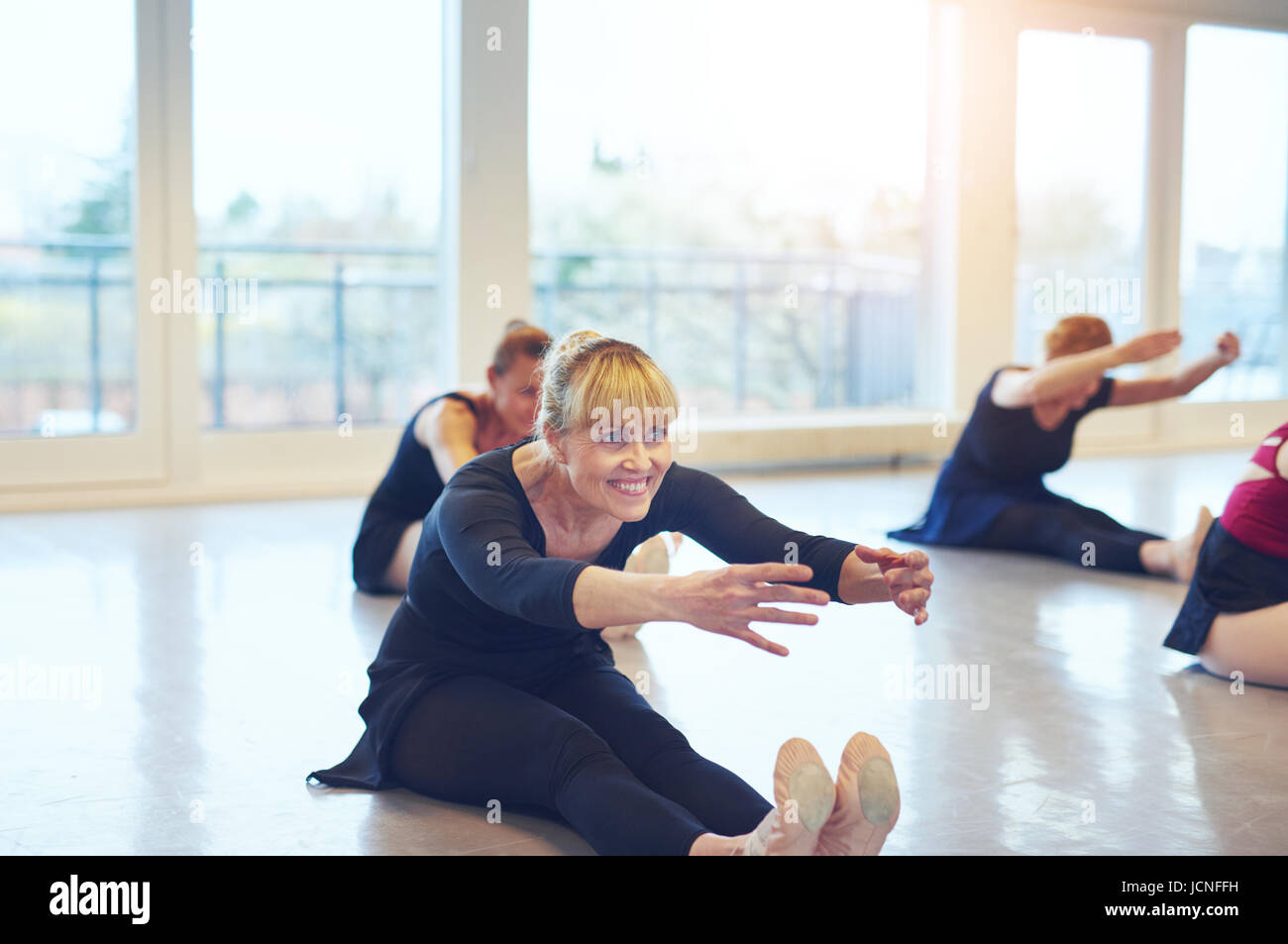 Fit smiling ballerinas sitting on floor and stretching while doing gymnastics in ballet class. Stock Photo