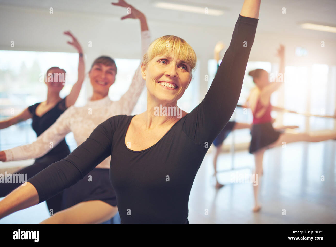 Cheerful smiling adult ballerina stretching with hand up performing a dance in ballet class. Stock Photo