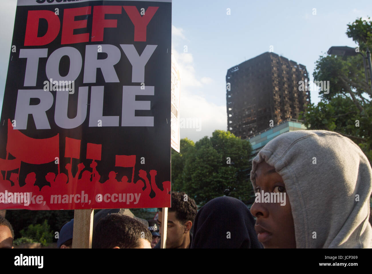 London, UK. 16th June, 2017. A man holds a placard 'Defy Tory Rule' in front of the shell of Grenfell Tower as as people demand justice for those affected by the fire that gutted Grenfell Tower, a residential tower block in west Lodon. Credit: Thabo Jaiyesimi/Alamy Live News Stock Photo
