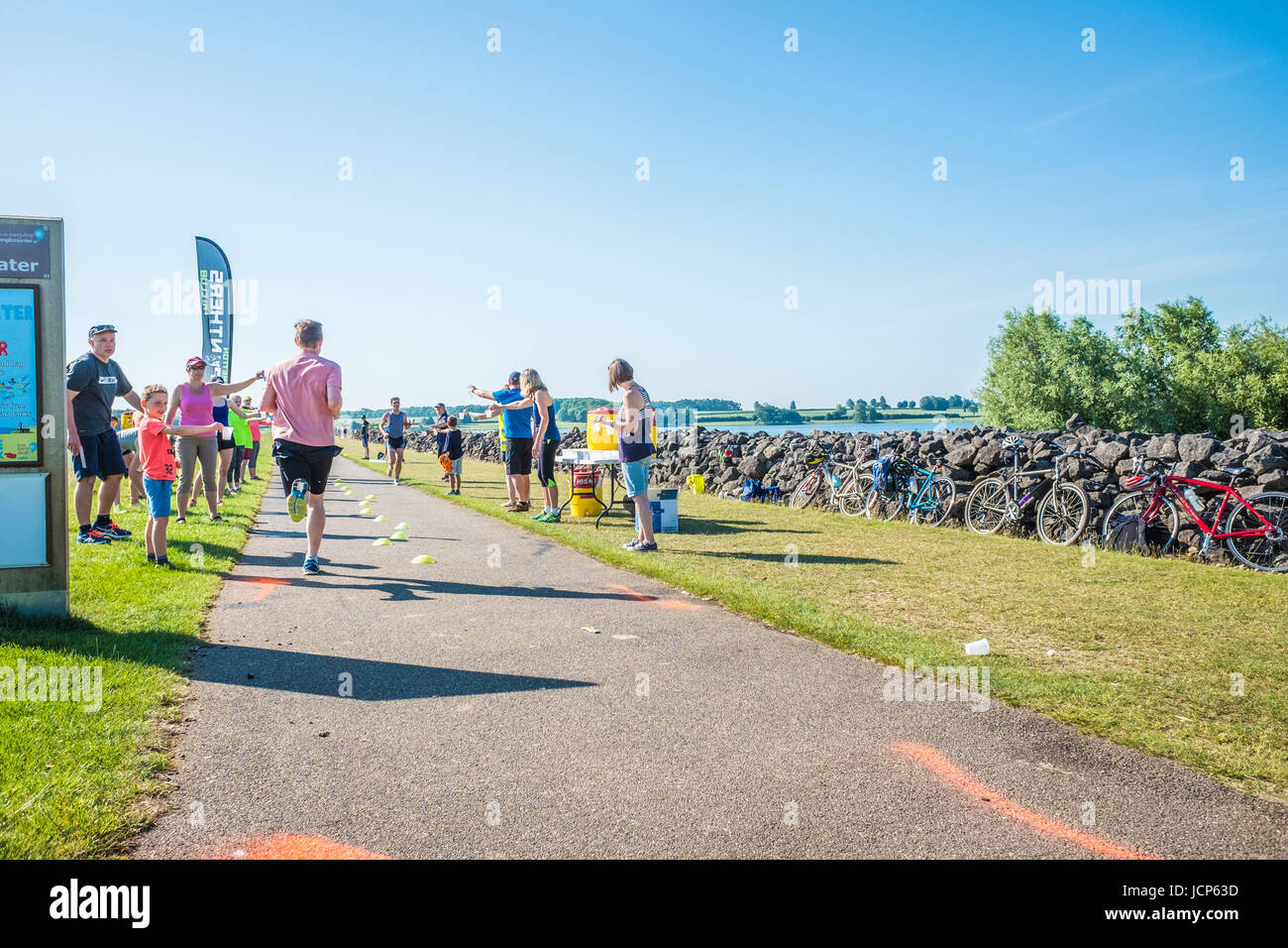 Rutland Water, UK. 17th June, 2017. Volunteers offer cups of water on a hot, sunny day at a drink point on the dam at Rutland reservoir during the10 km run, the third and final phase of the Dambuster Triathlon (swim, bike and run race) at Rutland Water, England, on 17 June 2017. Credit: Michael Foley/Alamy Live News Stock Photo