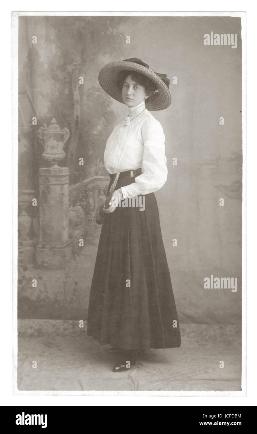 Postcard, studio portrait of pretty stylish, glamorous young Edwardian lady wearing large wide-brimmed hat and white high necked blouse and skirt typical of the era, holding a tennis racquet, circa 1910, Weymouth, Dorset, U.K. Stock Photo