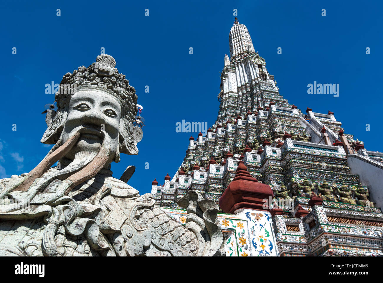 The sculpture of a smiling chinese man with the prang style Wat Arun buddhist temple in the city center of Bangkok, Thailand. Stock Photo