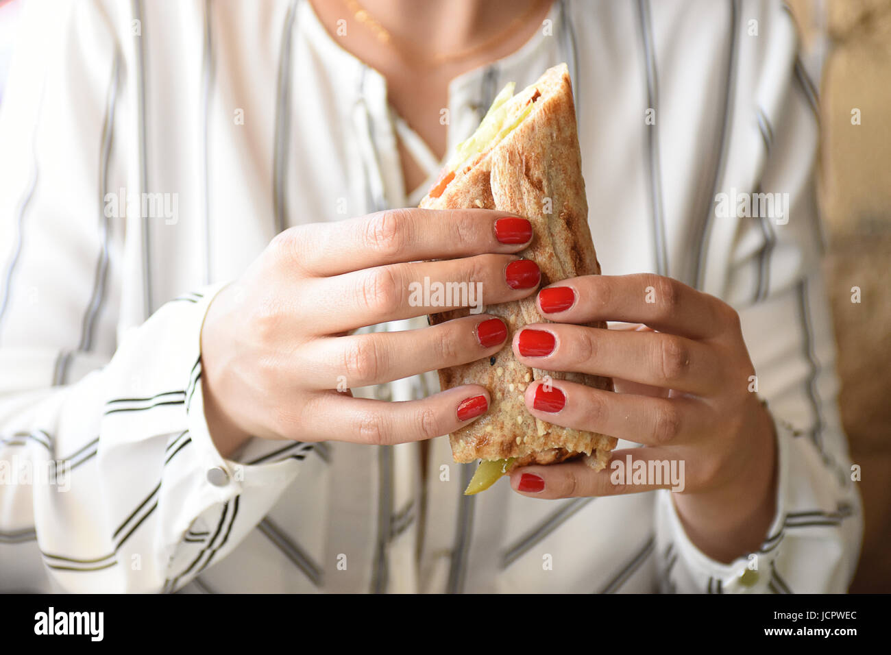 Woman with red nail polish eating a healthy wrap sandwich Stock Photo
