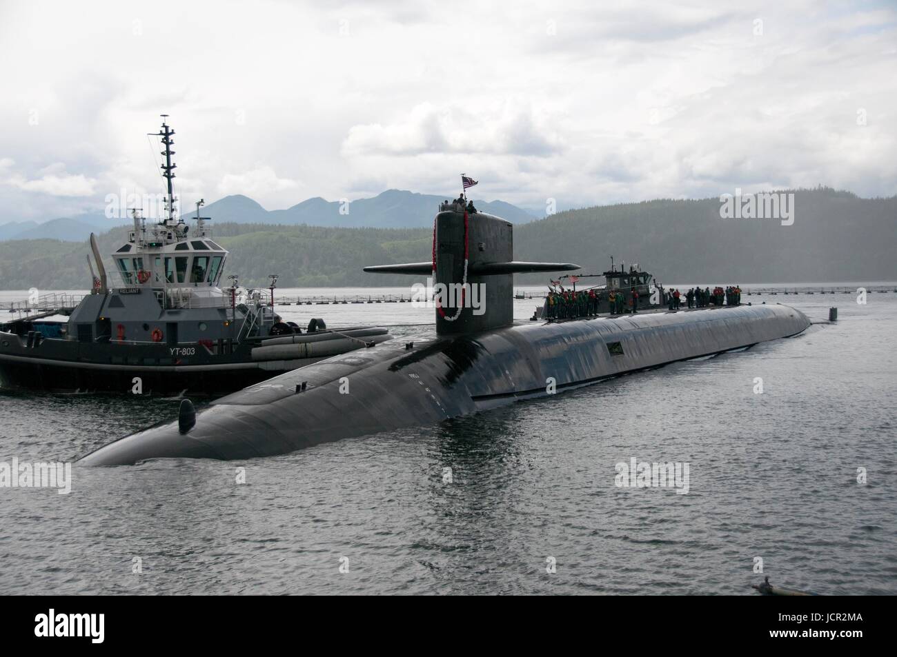 A tug boat pushes the USN Ohio-class ballistic-missile submarine USS Nebraska into dock as it returns to Naval Base Kitsap-Bangor June 9, 2017 in Bangor, Washington. Stock Photo