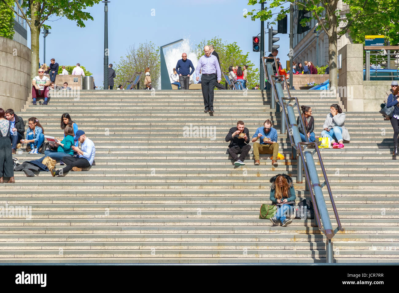 London, UK - May 10, 2017 - People sitting and eating on Cubitt Steps in Canary Wharf on a sunny day Stock Photo