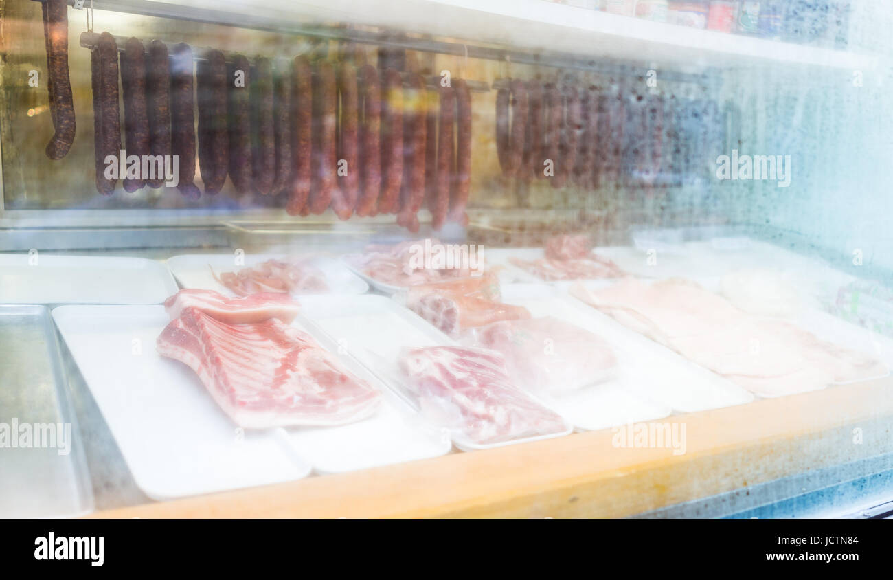 Sausages and raw cuts of meat closeup behind foggy window glass of