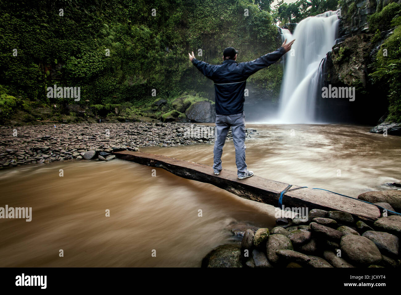 One man marvels at the wonders of a powerful hidden waterfall in natures stunning surroundings on the Indonesian island of Bali in Southeast Asia. Stock Photo