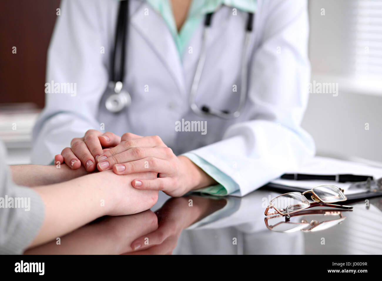 Friendly female doctor hands holding patient hand sitting at the desk for encouragement, empathy, cheering and support while medical examination. Bad  Stock Photo