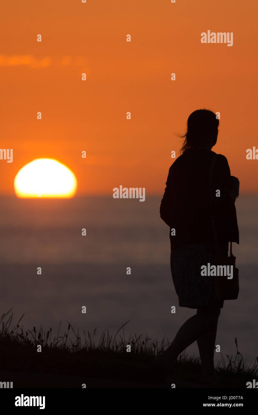 silhouetted people looking out to sea at sunset Stock Photo Alamy