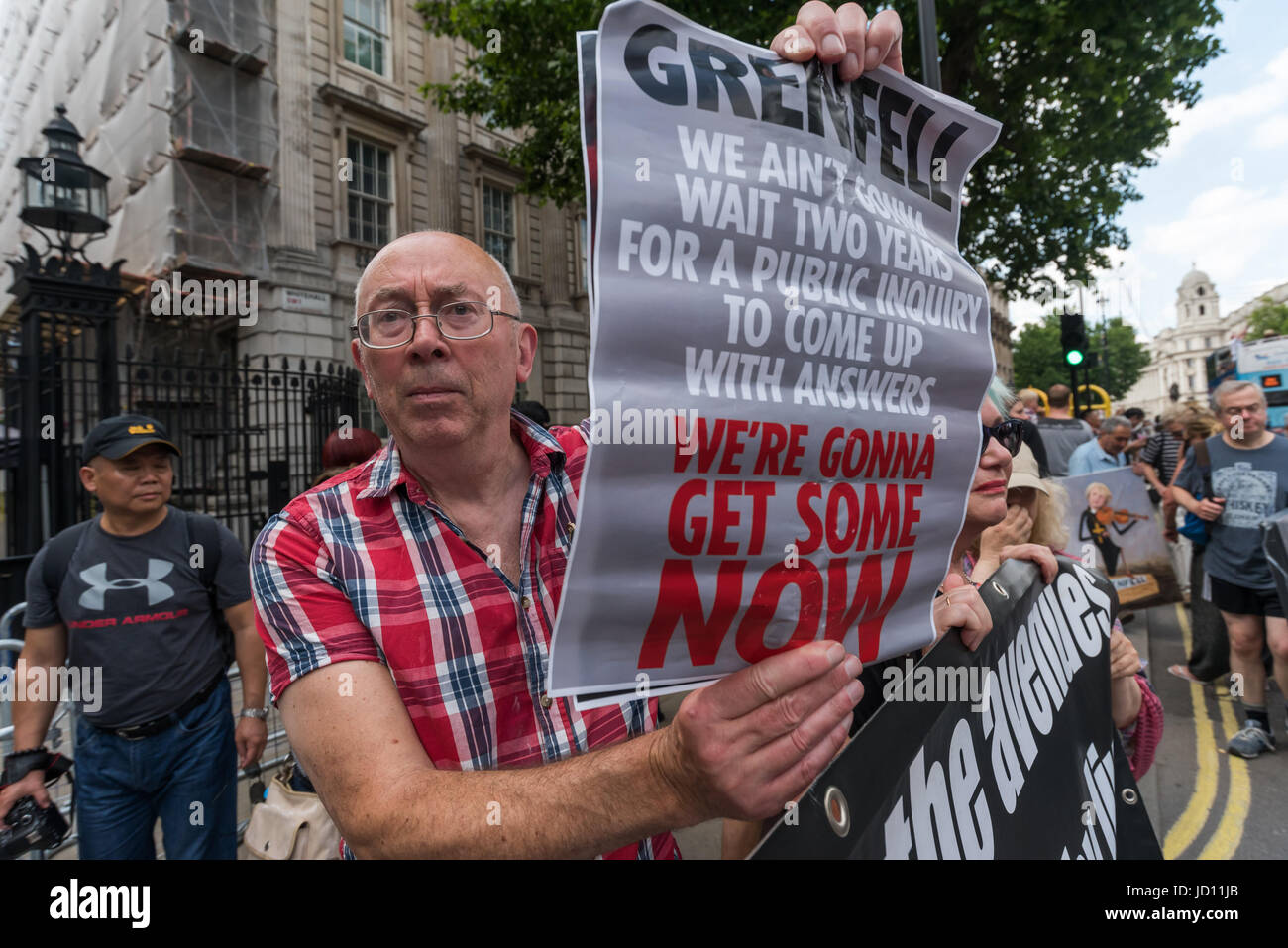 London, UK. 17th June, 2017. London, UK. 17th June, 2017. Ian BOne of Class War stands behind their banner outside Downing St facing the large protest across thr road calling on Theresa May to resign.He holds up a poster 'Grenfell - We ain't gonna wait two years for a public inquiry to come up with answers - We'e gonna get some NOW'. Peter Marshall Images Live Credit: Peter Marshall/ImagesLive/ZUMA Wire/Alamy Live News Stock Photo
