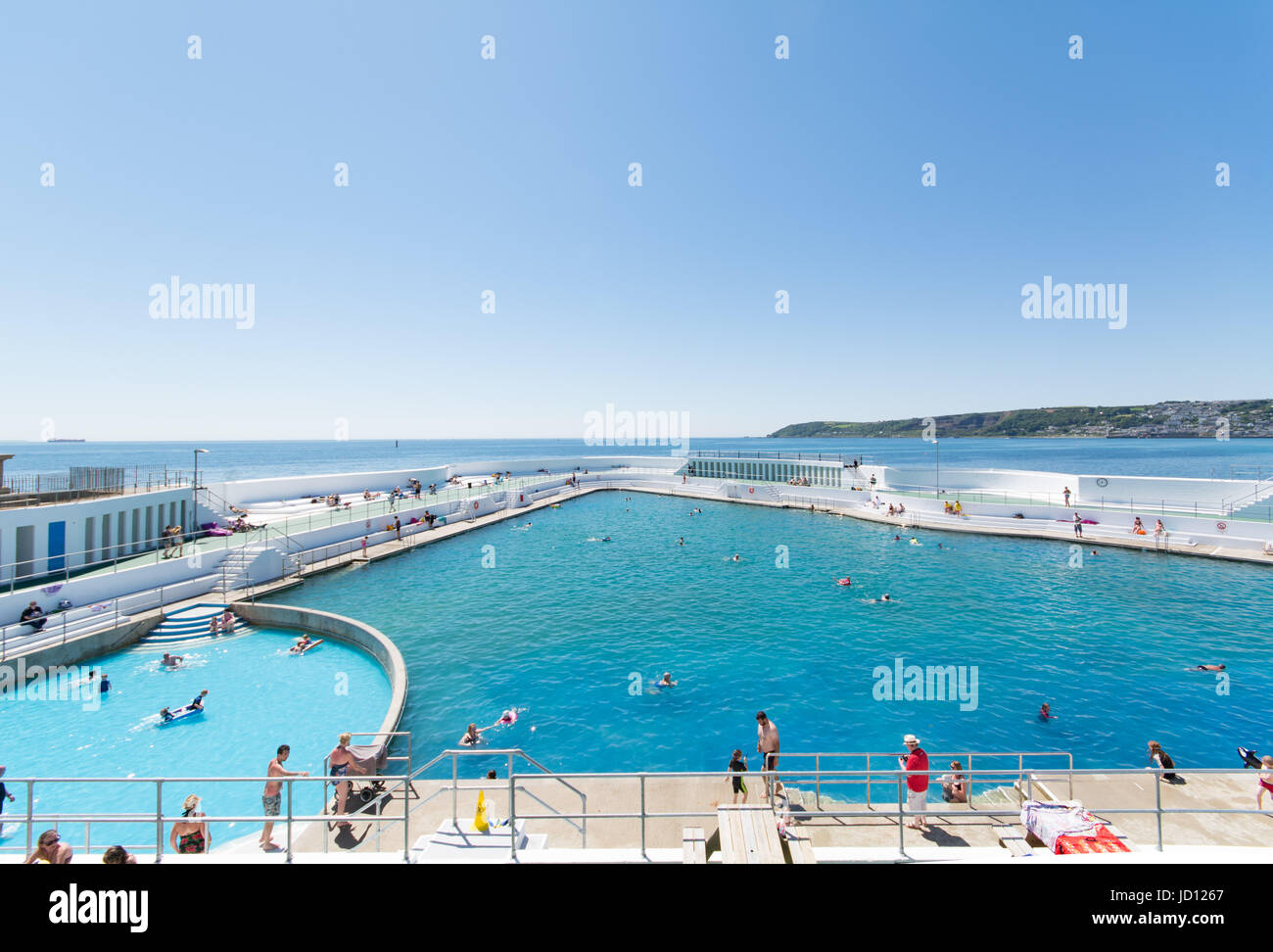 Penzance, Cornwall, UK. 18th June 2017. UK Weather. People colling off and sunbathing at the newly refurbished Jubilee Lido pool at Penzance, with views across Mounts bay towards Newlyn in the distance. Credit: cwallpix/Alamy Live News Stock Photo