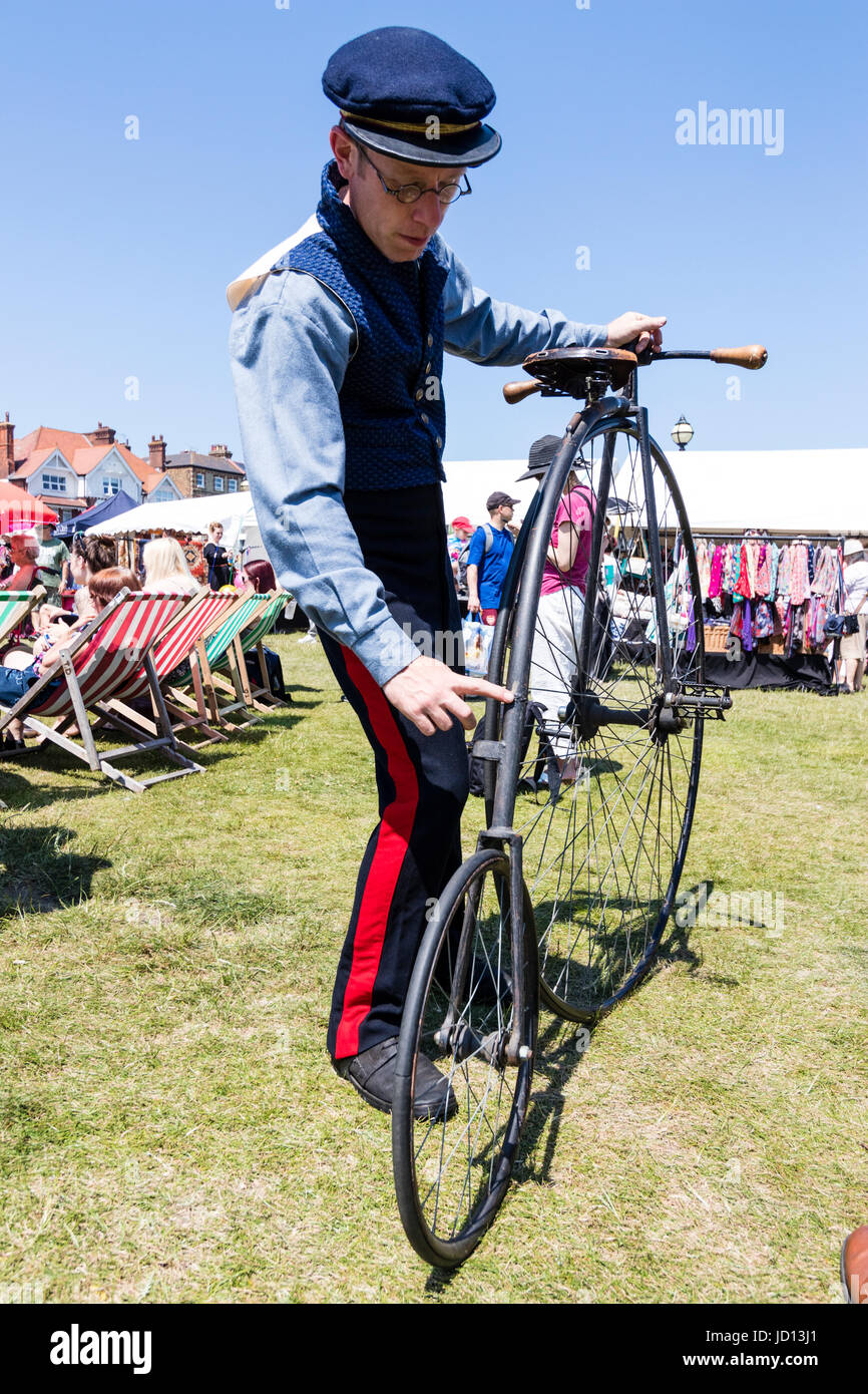 Man standing holding his penny farthing early Victorian bicycle on the grass during Broadstairs Dickens week. Wearing uniform and cap. Low angle view point. Stock Photo