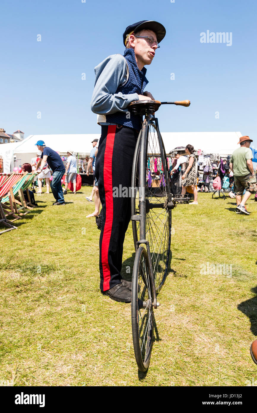 Man standing holding his penny farthing early Victorian bicycle on the grass during Broadstairs Dickens week. Wearing uniform and cap. Low angle view point. Stock Photo