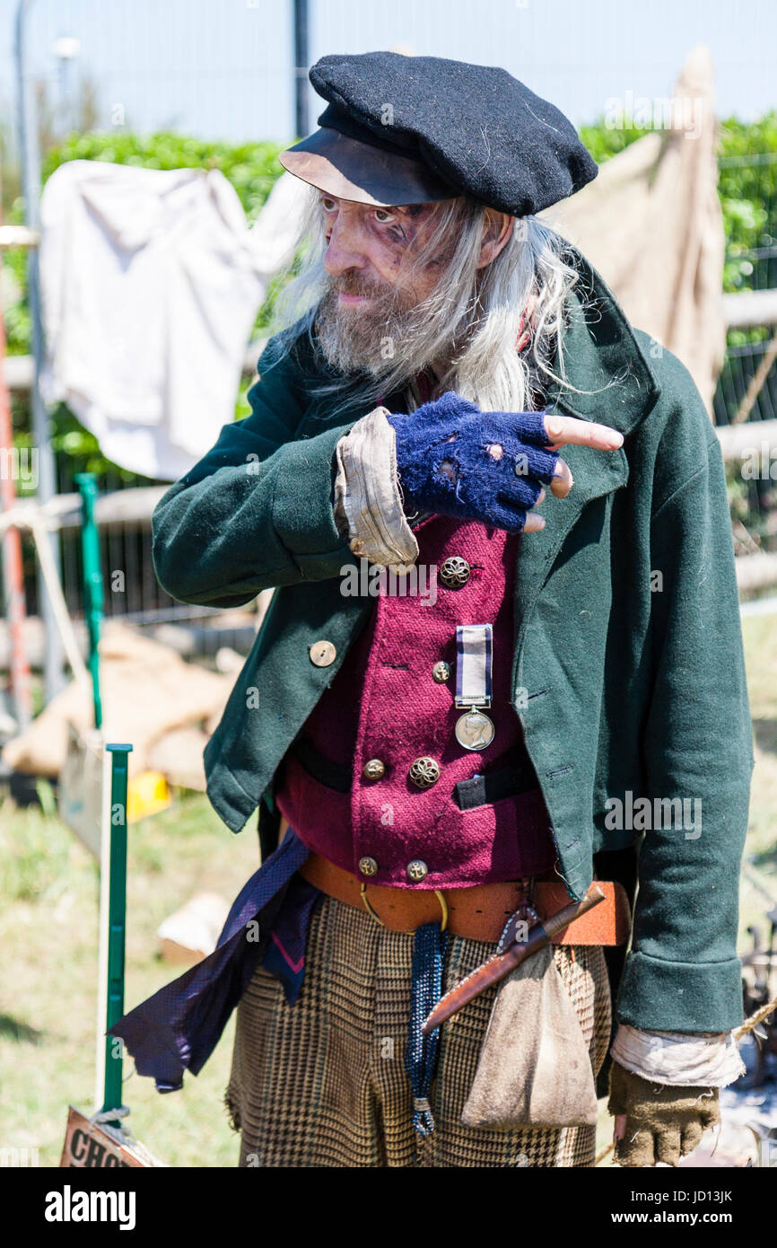 Down and out Navy, senior old man, Victorian character re-enactment. Filthy dirty wears green jacket, red waistcoat and medal. Talking and pointing. Stock Photo
