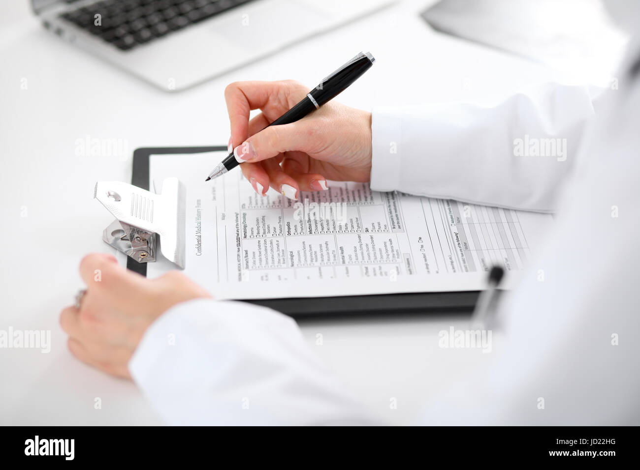Close-up of a female doctor filling out application form , sitting at ...