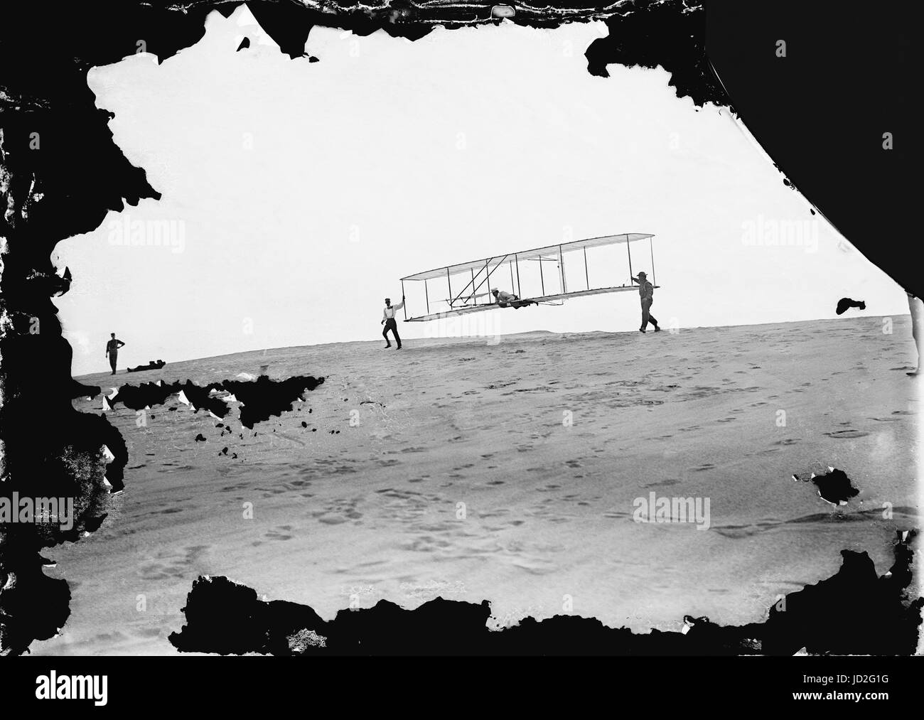 Start of a glide; Wilbur in motion at the left holding one end of glider (rebuilt with single vertical rudder), Orville lying prone in machine, and Dan Tate at right; Photographed  October 10, 1902, Kitty Hawk, North Carolina. The photograph was made on a 5' x 7' dry glass plate and is attributed to Wilbur and/or Orville Wright. Stock Photo