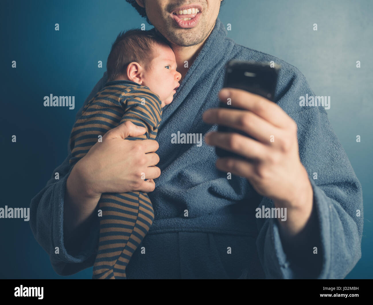 A young father in a bathrobe is taking a selfie with his baby son Stock
