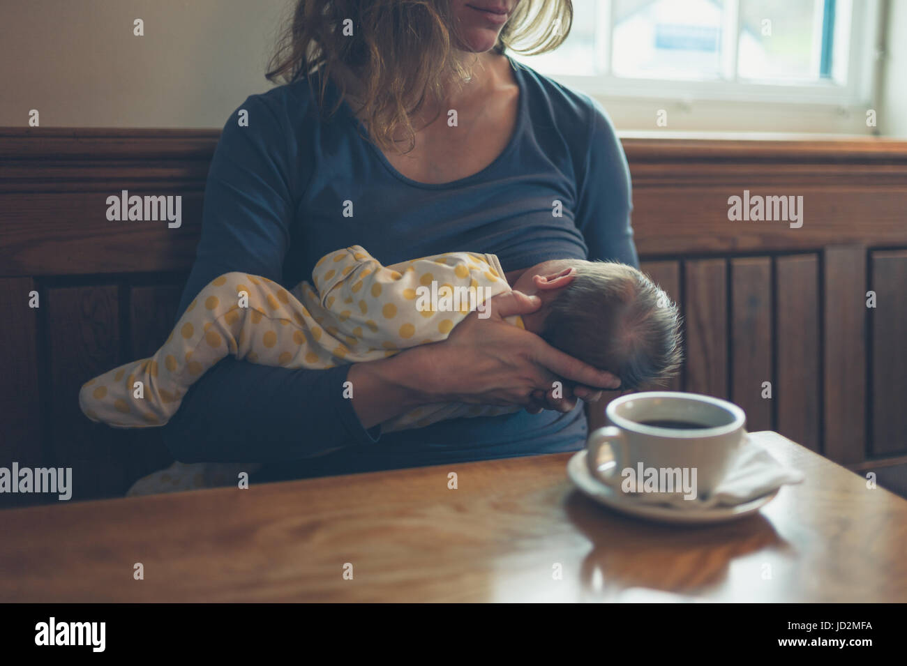 A young mother is breastfeeding her baby in a cafe while she is having a coffee Stock Photo