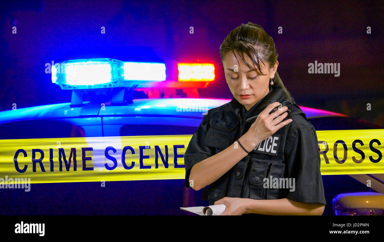 Asian American Policewoman using police radio with siren and boundary tape in background Stock Photo