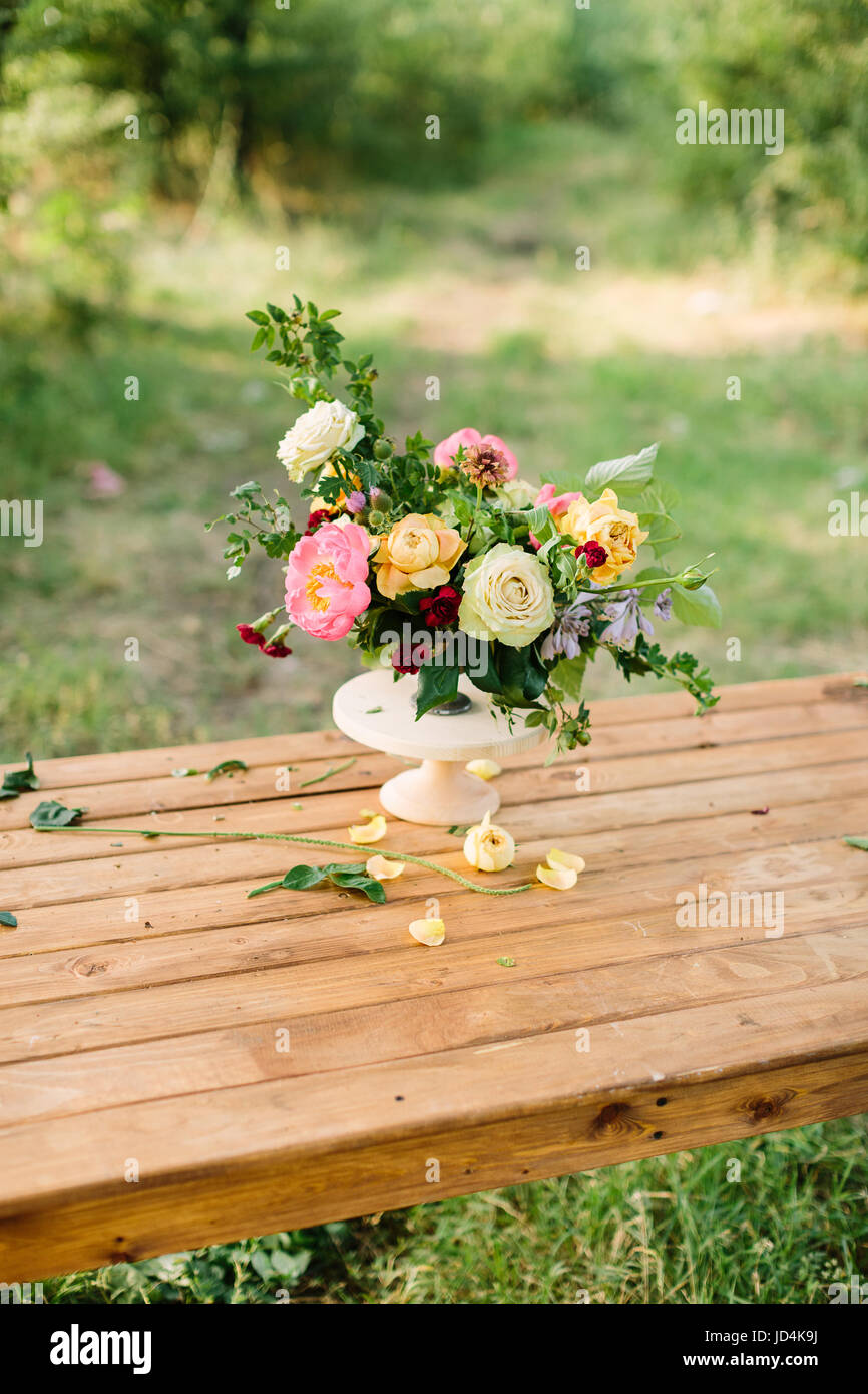 floral design, wedding, romance concept - gorgeous bouquet made of tender avalanches, roses, peonies and dianthuses, decorated with leaves of oak and raspberry-bush, standing in vase on wooden table Stock Photo
