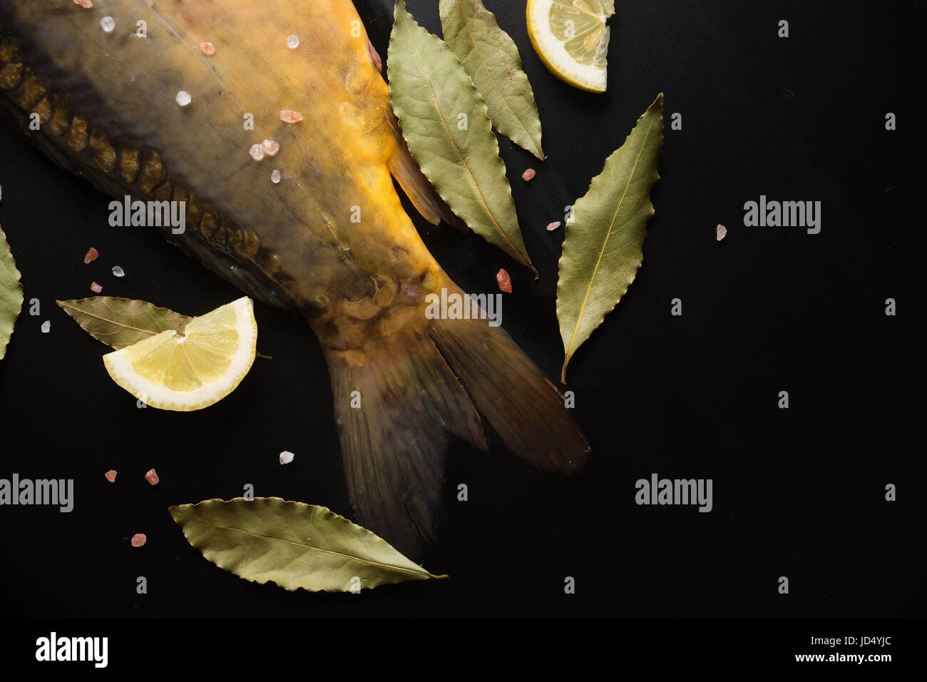 Top view of raw carp tail with lemon slices and bay leaves on black background with copy space for your text. Stock Photo