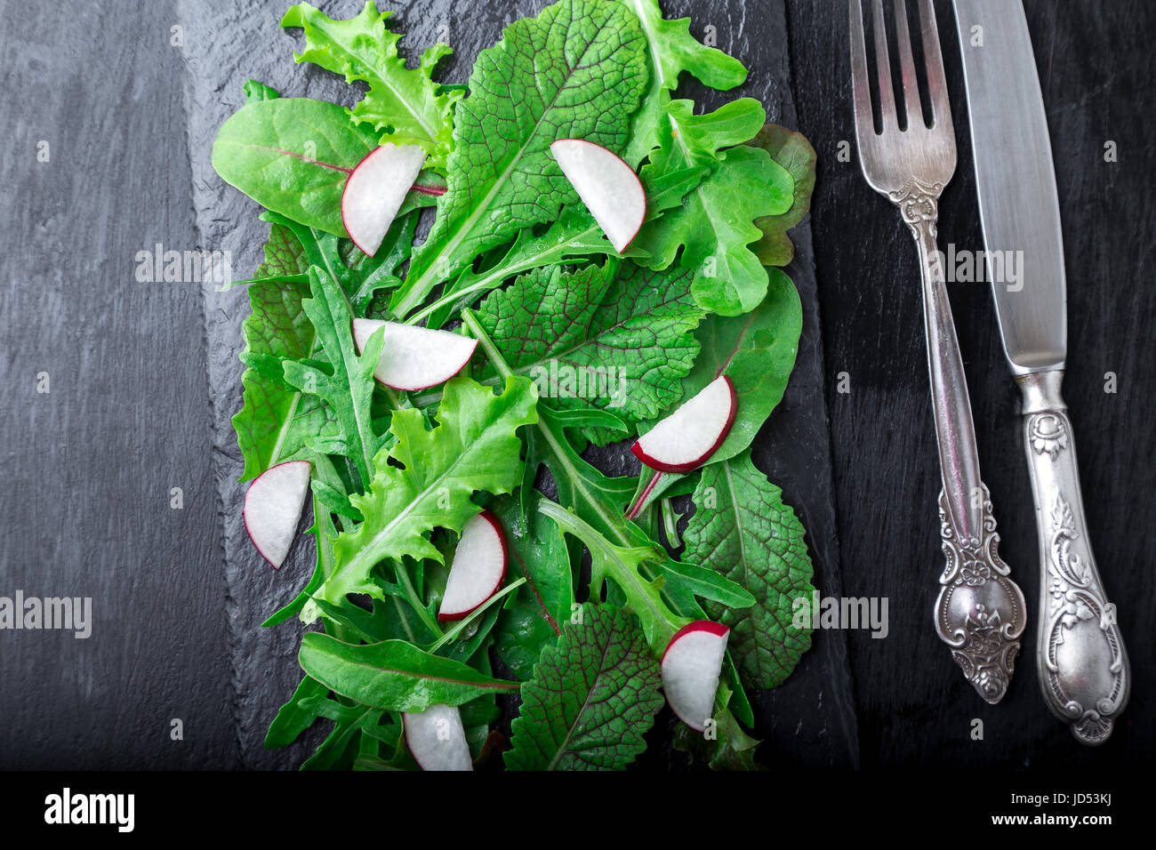 Mixed salad leaves with radish on black slate plate. Top view Stock Photo