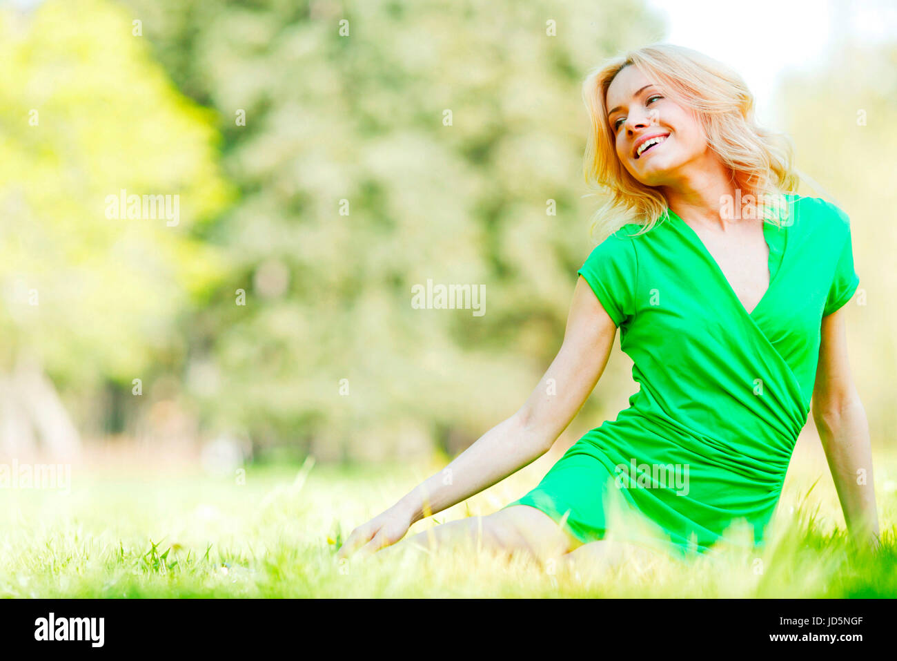 Beautiful young blond woman sitting on grass in park Stock Photo - Alamy