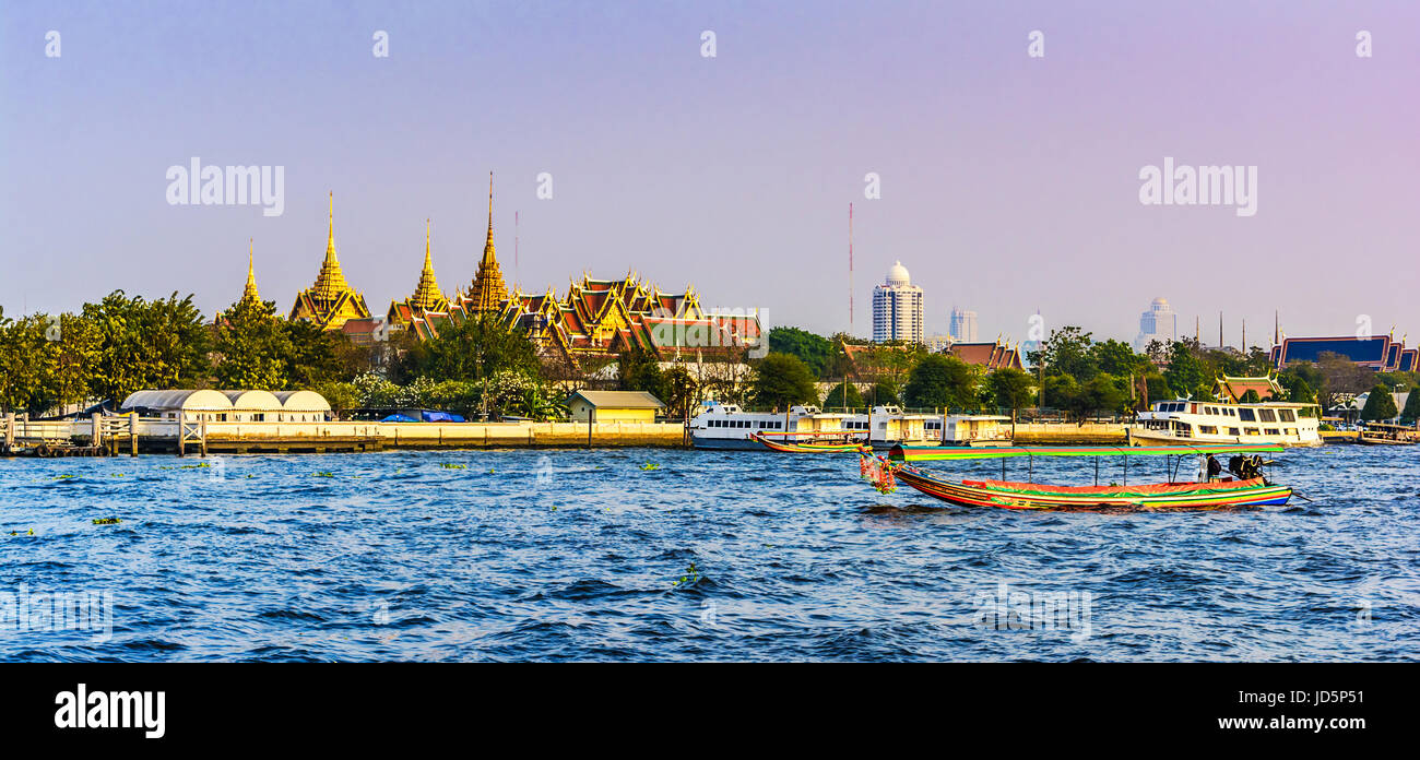 Sunset view across the Grand Palace, with the Chao Praya River and colorful boats in the foreground, Bangkok,Thailand Stock Photo
