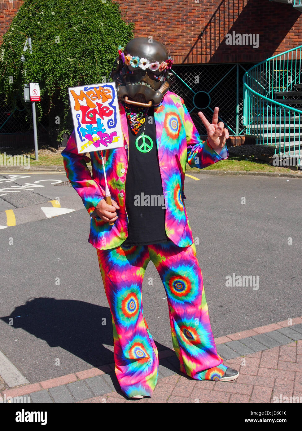 A man wearing a dark storm trooper helmet and wearing a psychedelic  suit carries a sign saying 'Make love not Star Wars' Stock Photo
