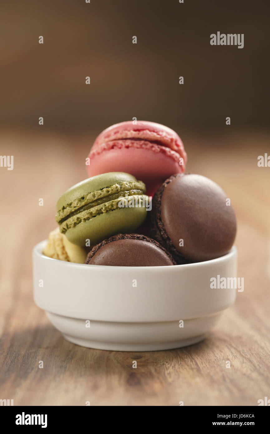 assorted macarons in white bowl on wooden table Stock Photo