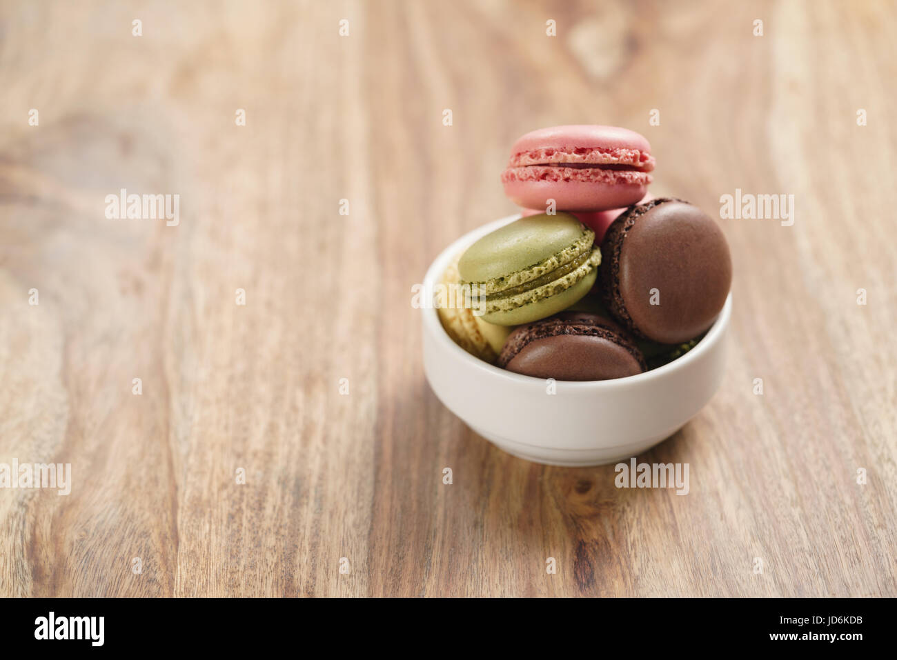 assorted macarons in white bowl on wooden table Stock Photo