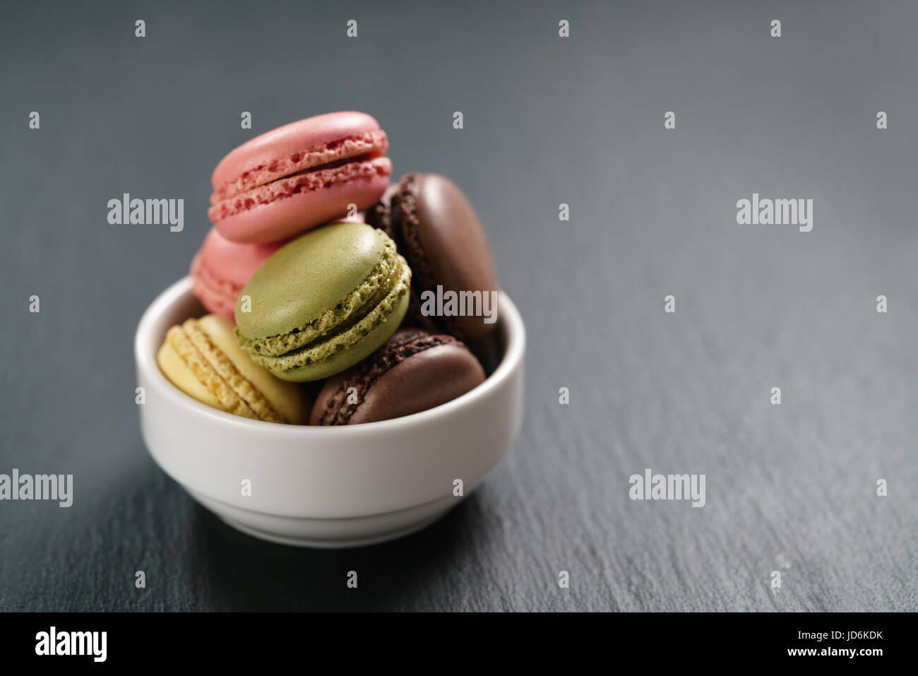 assorted macarons in white bowl on slate background Stock Photo