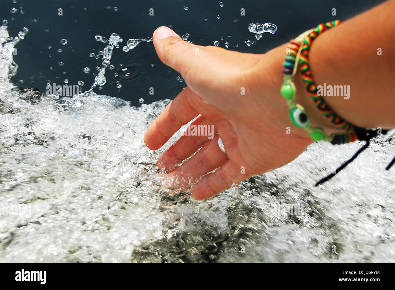 Female hand touching splashes of foaming water while floating on engine boat. Close-up picture. Stock Photo