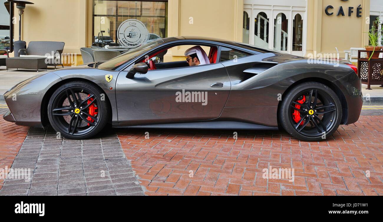 A young man in traditional Qatari outfit checks his cell phone inside his Ferrari sports car in front of a restaurant in Doha, the capital of Qatar Stock Photo