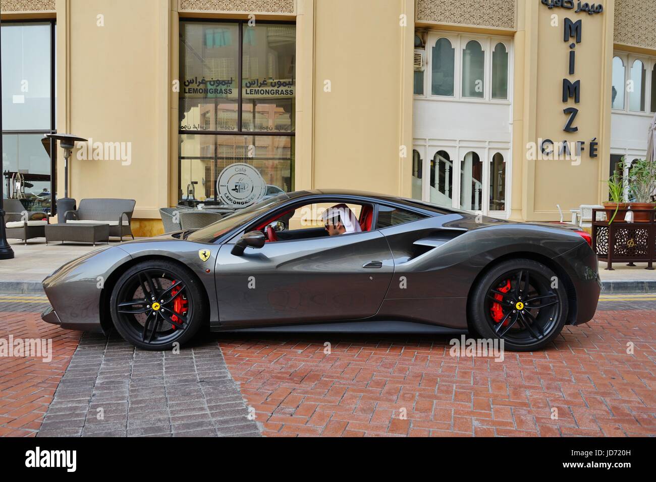 A young man in traditional Qatari outfit checks his cell phone inside his Ferrari sports car in front of a restaurant in Doha, the capital of Qatar Stock Photo
