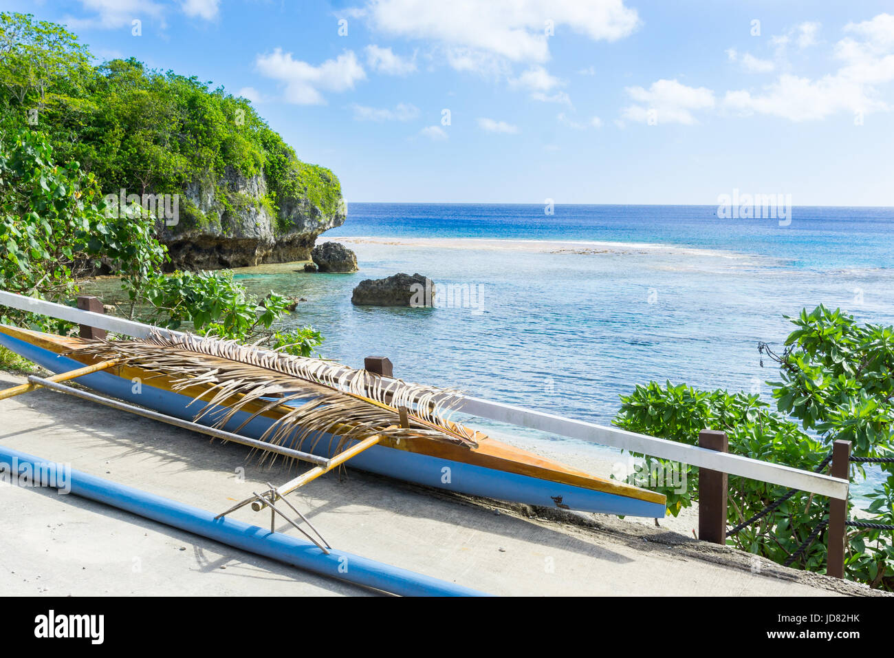 Out-rigger canoe under palm frond to shield some rainwater from boat on ledge overlooking scenic coastline and vast Pacific Island, Niue. Stock Photo