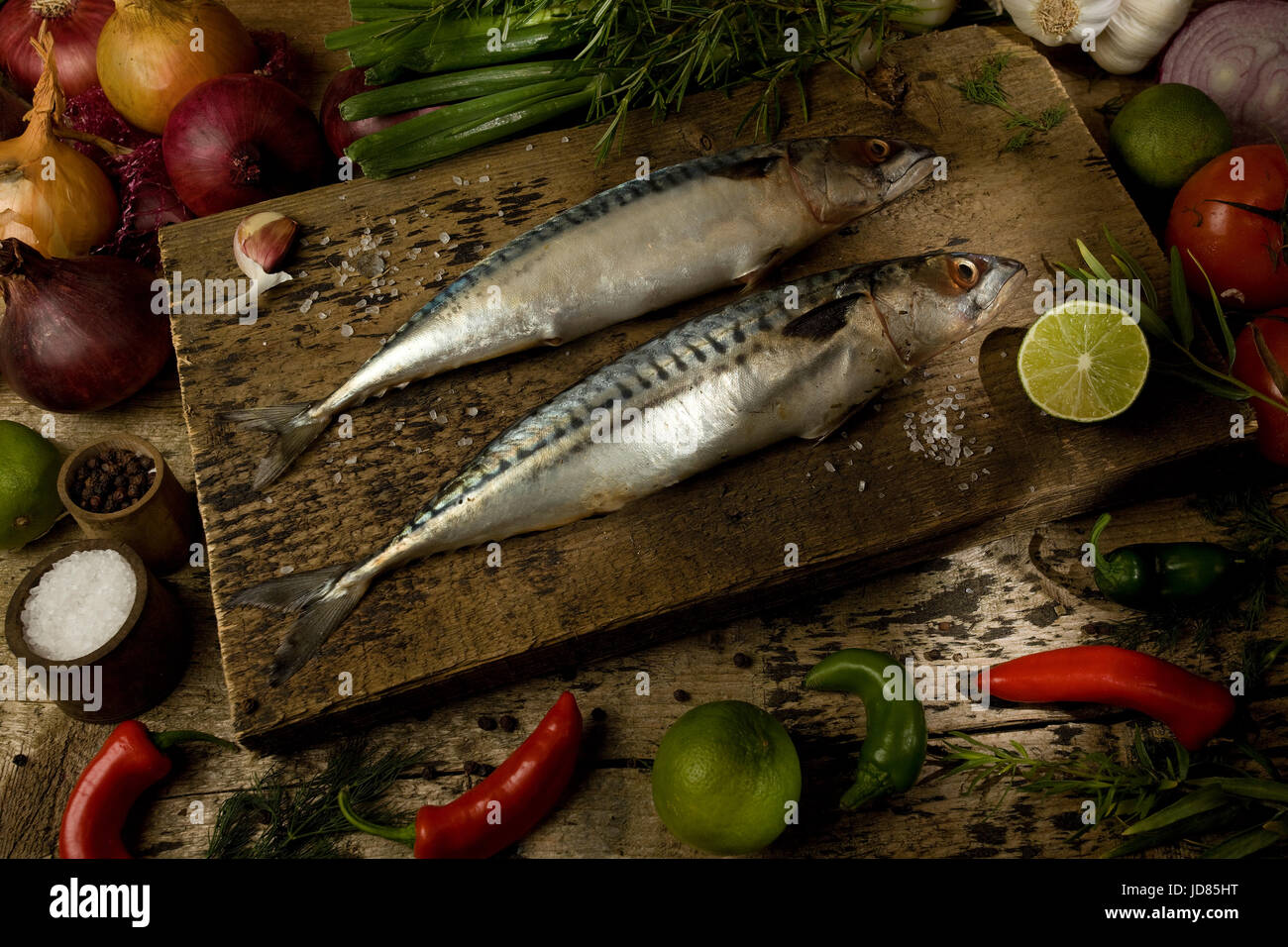 Two whole mackerel on chopping board with raw ingredients Stock Photo