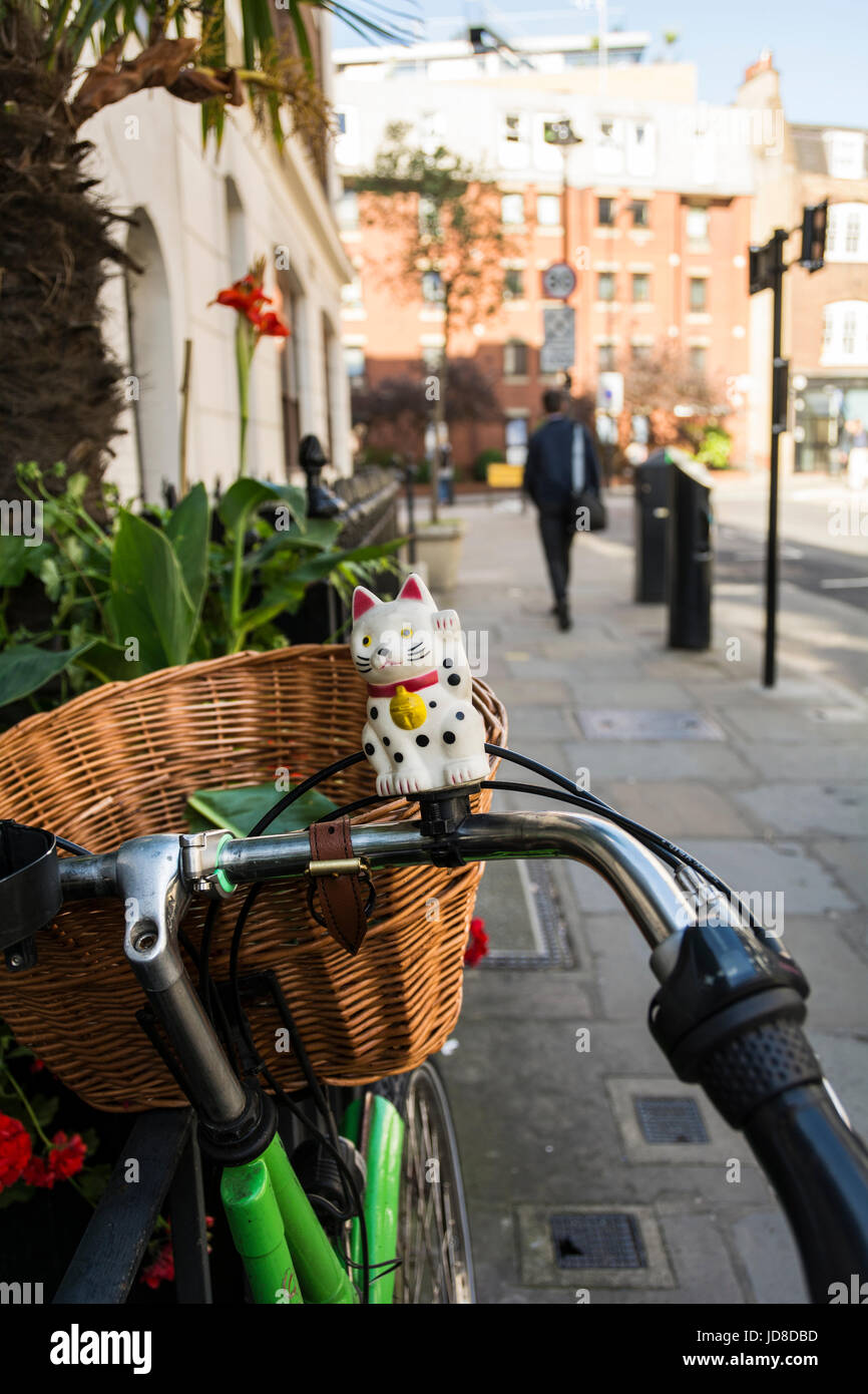 Maneki Neko (Japanese beckoning cat) on a bicycle in Fitzrovia, London, UK Stock Photo