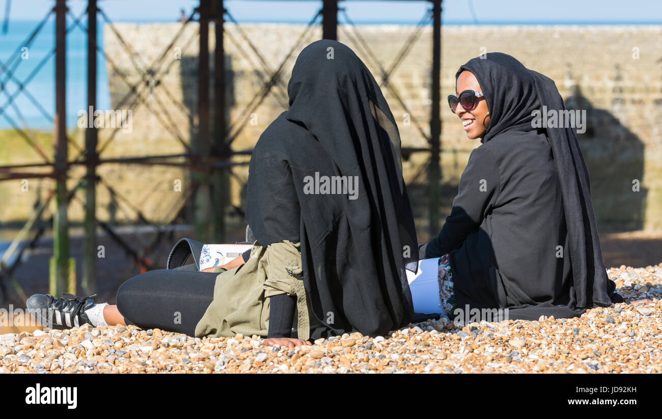 Young women wearing a black Chador while sitting on a shingle beach on a hot sunny day. Stock Photo