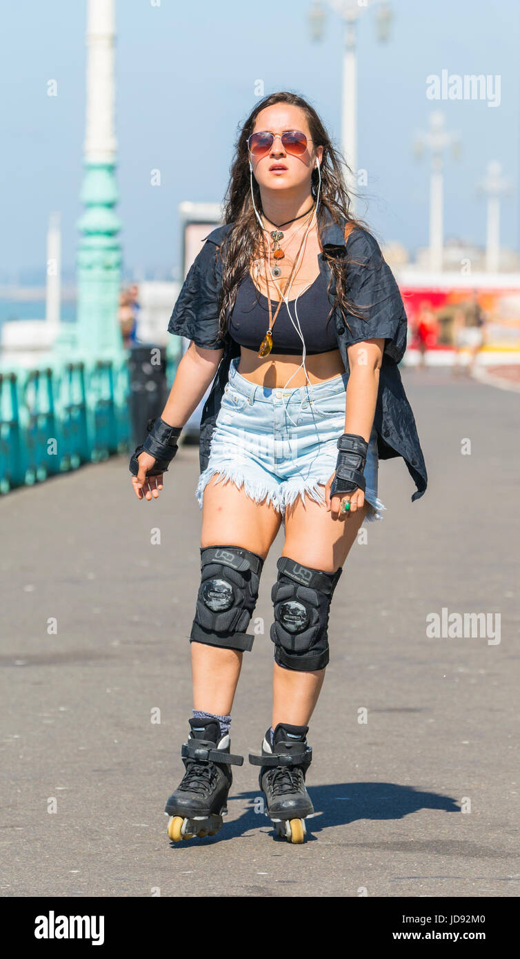 Young woman dressed for summer roller blading along the seafront promenade while listening to music, on a hot sunny day. Stock Photo