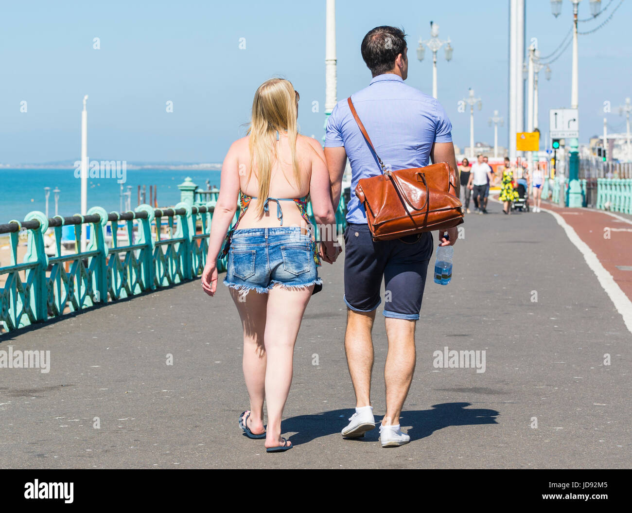 Young couple walking along a seaside promenade holding hands on a very got summers morning in the UK. Stock Photo