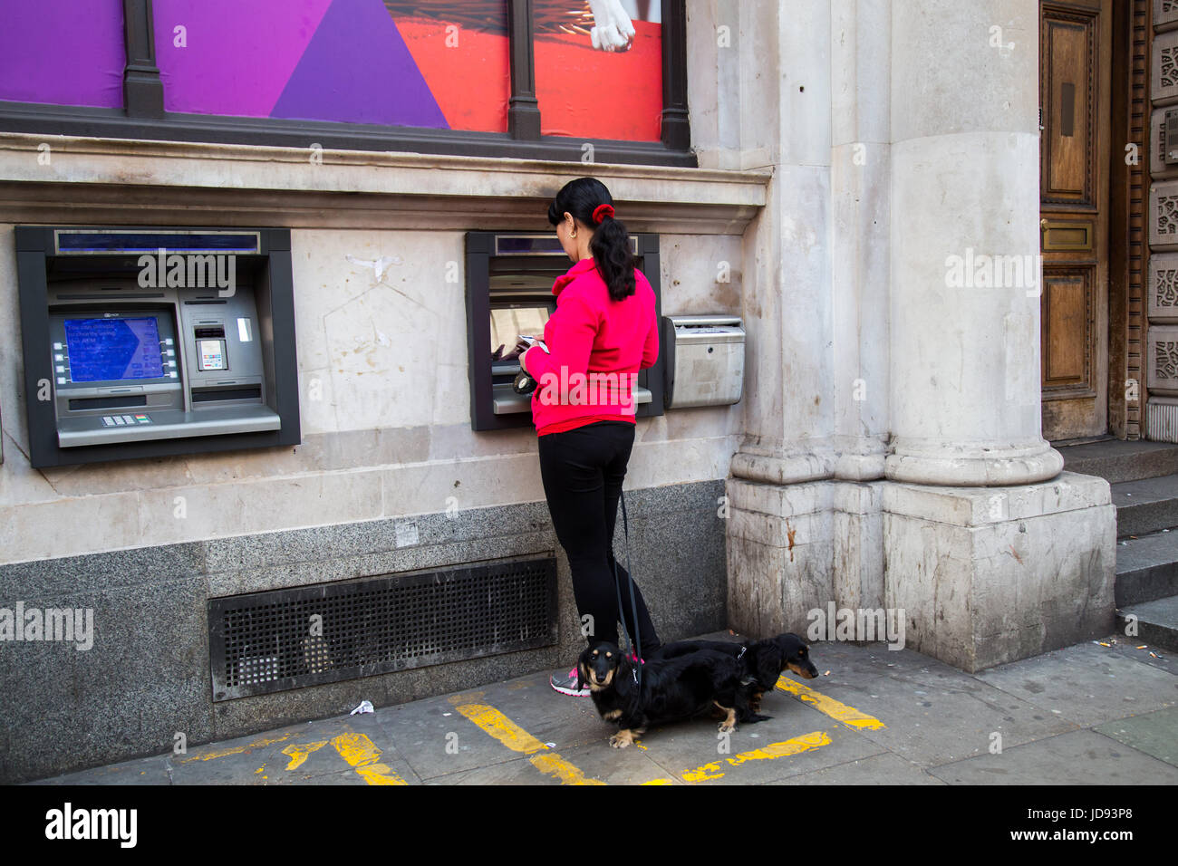 UK, London - April 08, 2015: A woman is standing by an ATM with dogs Stock Photo