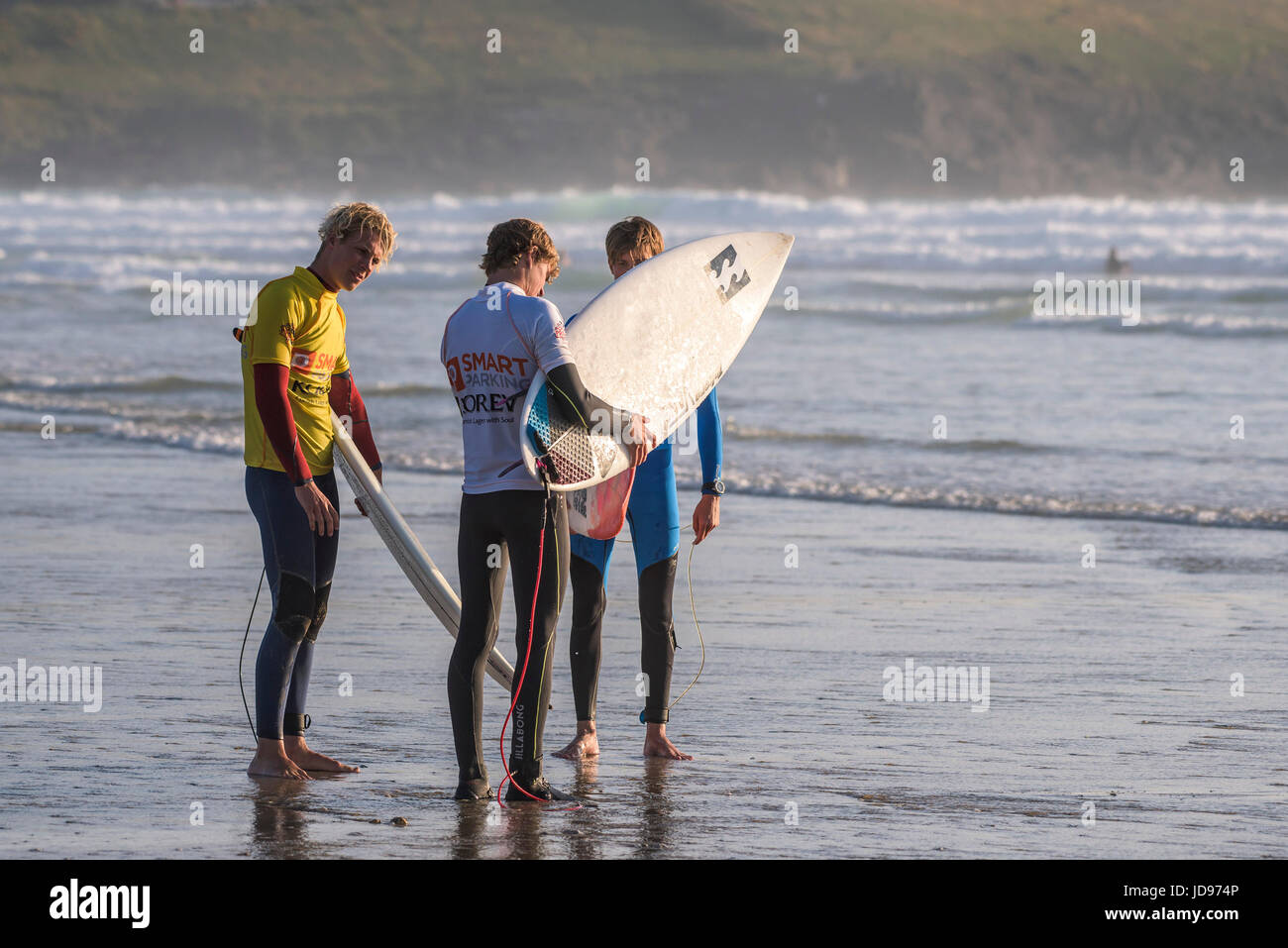 Three surfers standing on the shoreline before they enter the sea.  Fistral beach, Newquay, Cornwall. Stock Photo