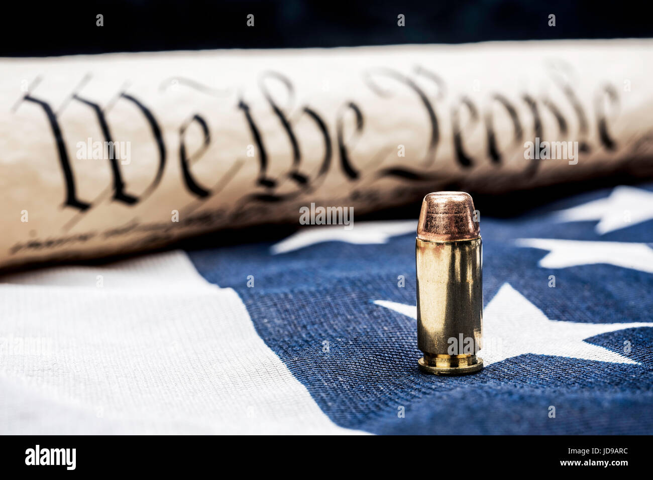 The United States Constitution rolled up next to a bullet rests on an American flag and symbolizes the right to bear arms. Stock Photo