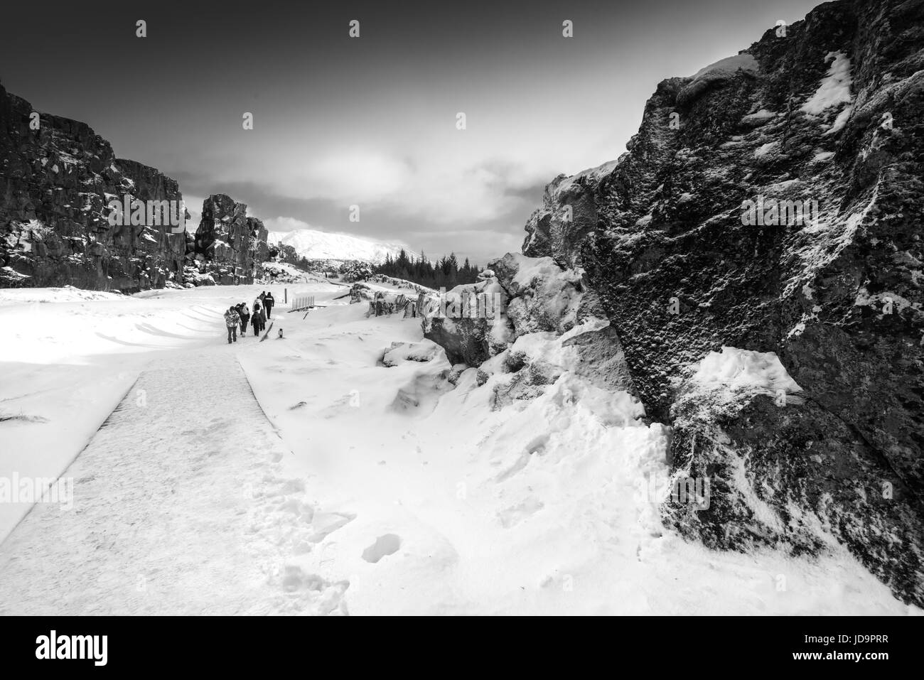 Small group of people walking on snow covered pathway by rock formations, Iceland, Europe, black and white. Iceland nature 2017 winter cold Stock Photo