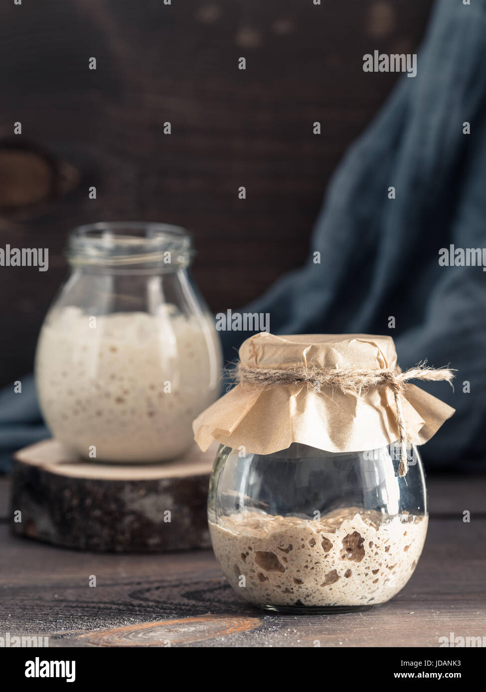 Active rye and wheat sourdough starter in glass jar on brown wooden