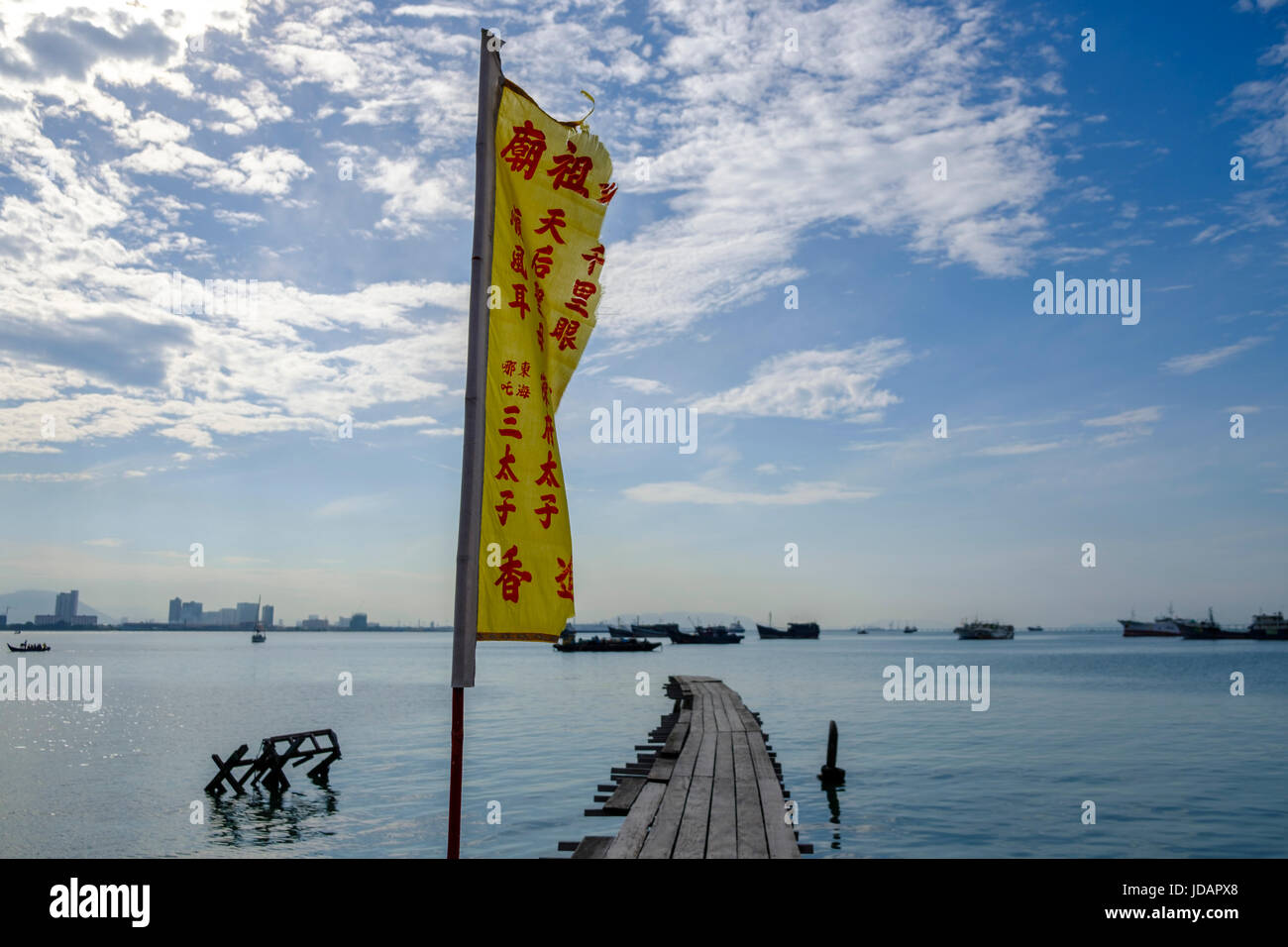 View of Penang harbour and the boardwalk and flag of Tan Jetty, one of the six Chinese Clan Jetties of Penang, Pulau Pinang, Malaysia. Stock Photo