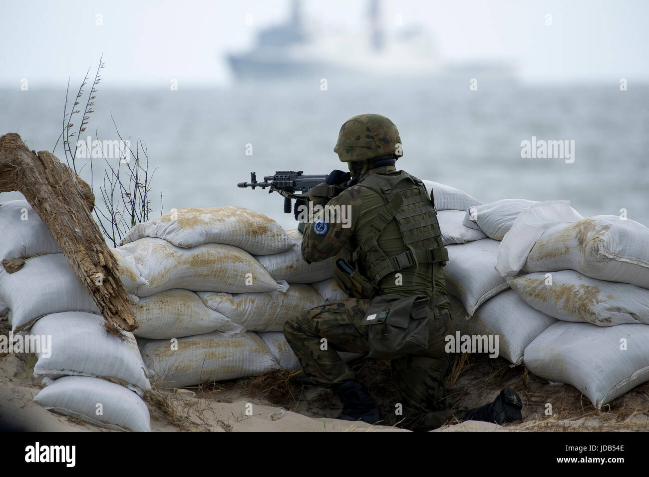 Polish soldier on the beach and in the back an American San Antonio class amphibious transport dock USS Arlington LPD-24 during the 45th edition of Ex Stock Photo